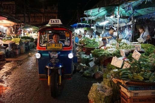 Tuk tuk driving past market vendors at night