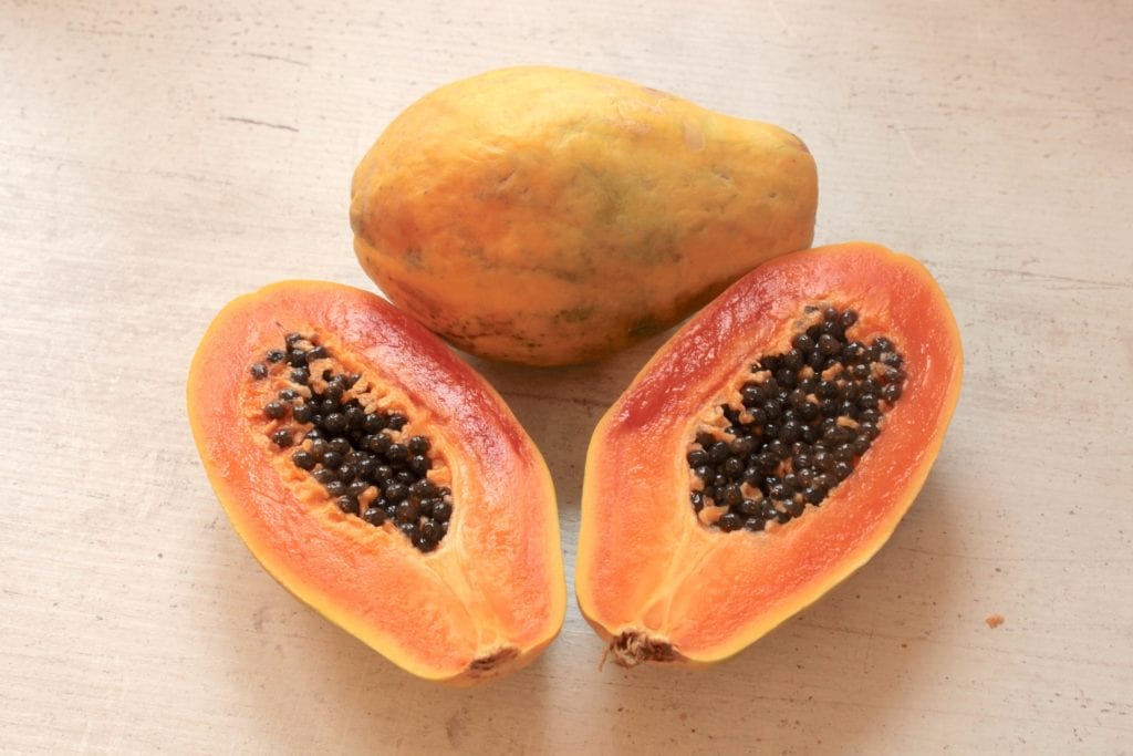 Image of 2 ripe papayas, one of the, is sliced showing orange fresh and lots of black seeds